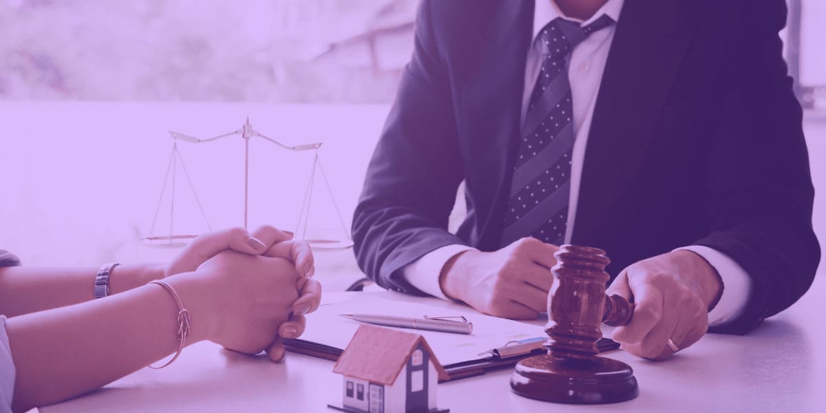 Modelo-de-Contrato-de-Locacao-Residencial A imagem mostra um ambiente formal, onde um advogado ou mediador jurídico está conversando com um cliente. Sobre a mesa, há um pequeno modelo de casa, representando simbolicamente um acordo imobiliário. Ao lado, um martelo de juiz e uma balança da justiça ao fundo reforçam a seriedade da situação. A cena sugere uma reunião para a formalização de um acordo, como a assinatura de um Modelo de Contrato de Locação Residencial, essencial para regulamentar a relação entre locador e locatário, garantindo direitos e deveres de ambas as partes no uso de um imóvel residencial.