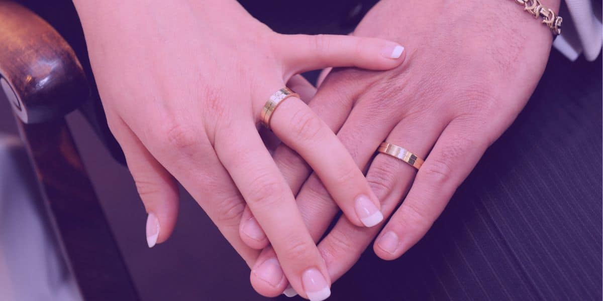 comunhao-universal-de-bens Um casal com as mãos juntas e alianças de casamento no dedo, simbolizando a comunhão universal de bens.