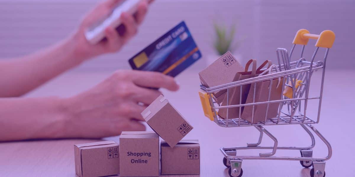 direito-de-arrependimento-art-49-cdc Uma pessoa mexendo no celular e, na outra mão, segurando um cartão de crédito. Ao lado, caixas de compras e um carrinho com compras dentro.